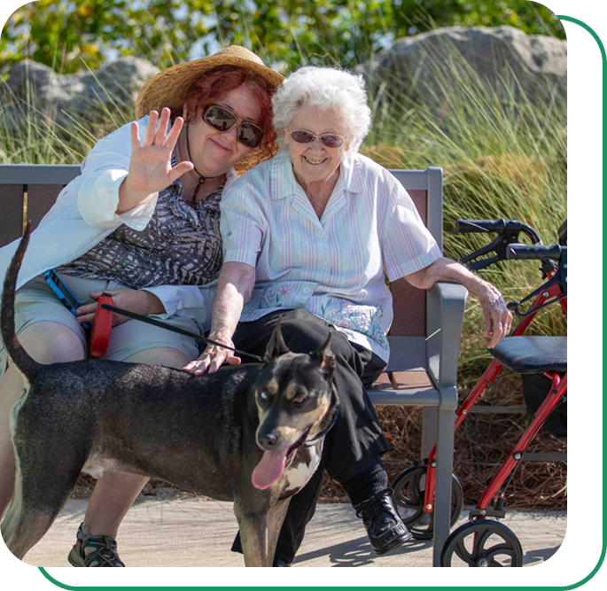Two older woman sitting on a park bench with their dog